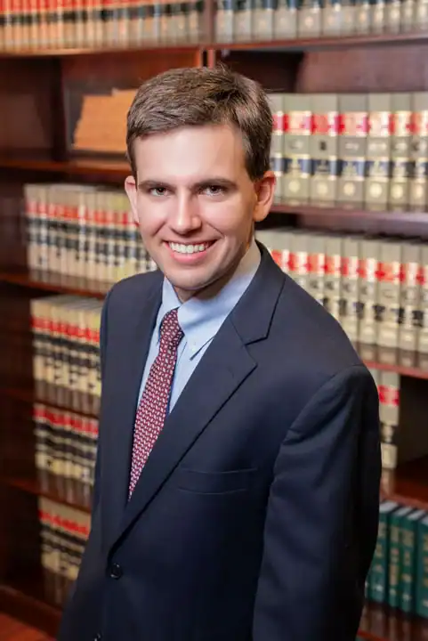 Young male lawyer in suit smiling in law library with legal books.